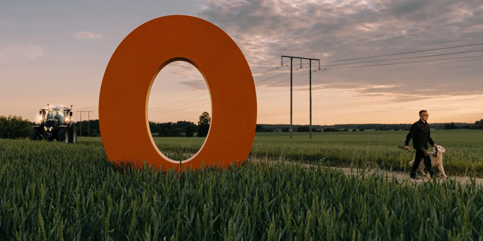 En man rastar en hund på ett fält bredvid ett stort orange föremål.