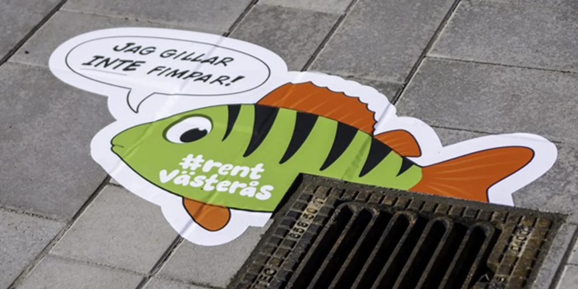 Ett klistermärke av en fisk på marken bredvid ett avlopp.