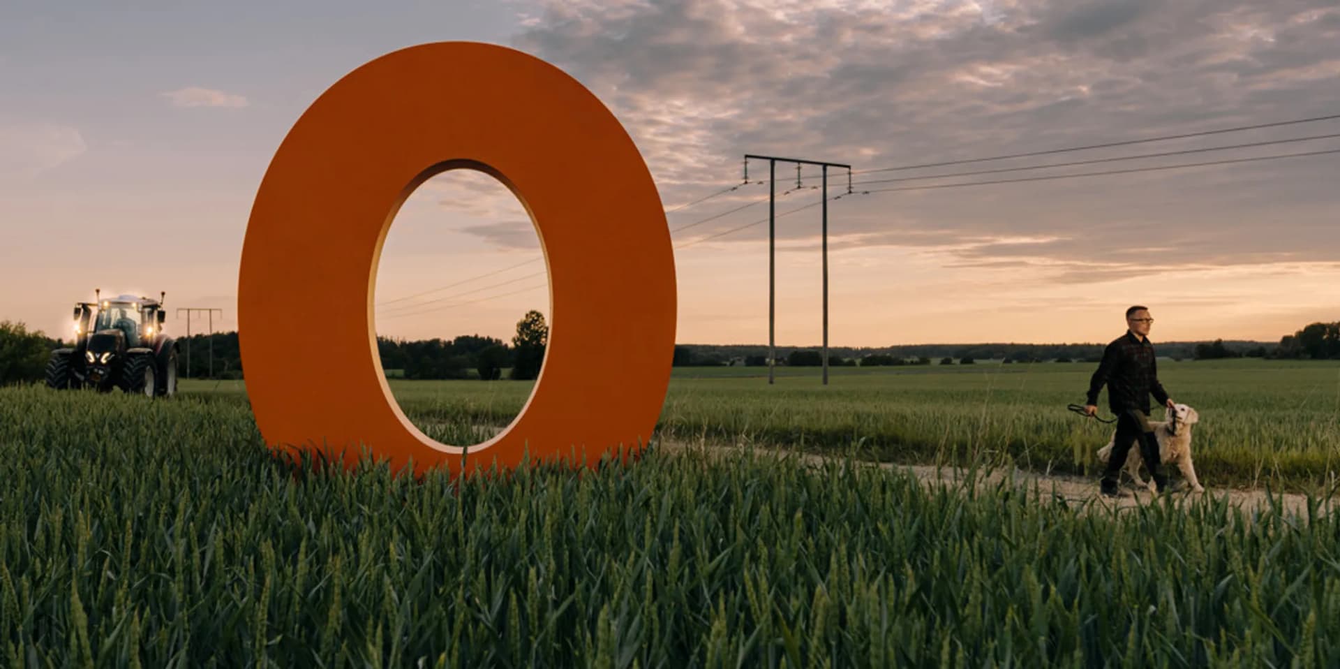En man rastar en hund på ett fält bredvid ett stort orange föremål.