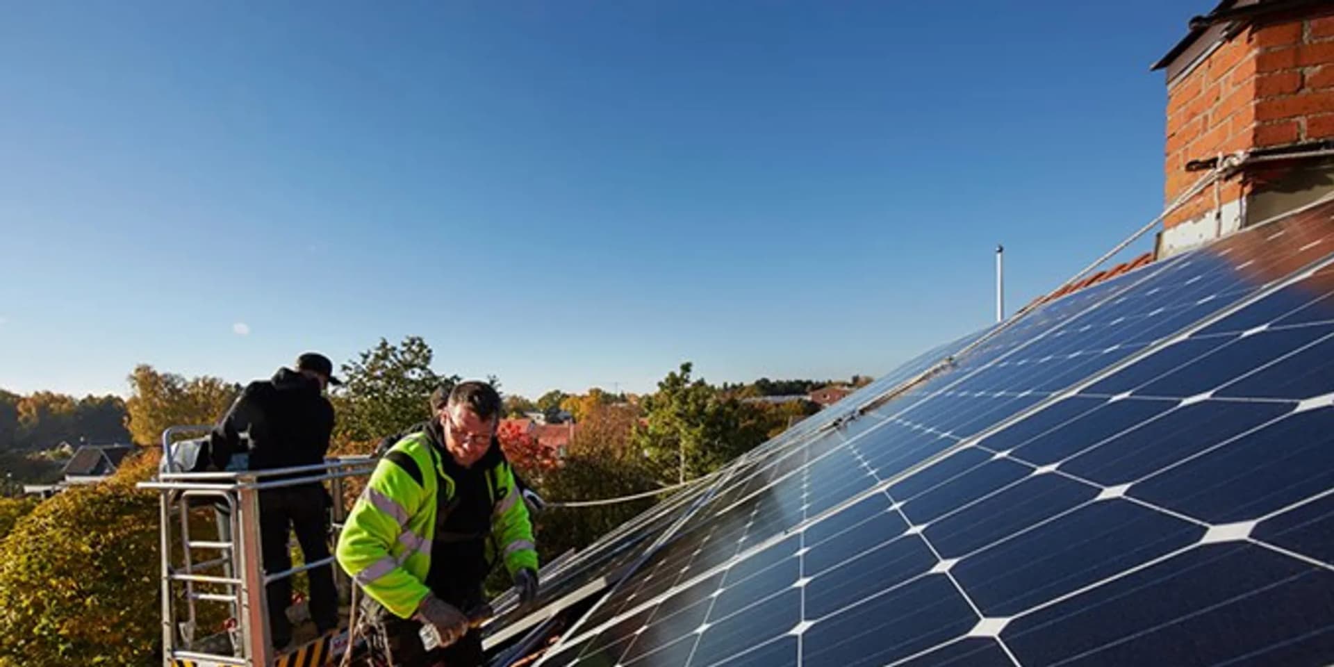 En man installerar solceller på taket till ett hus.