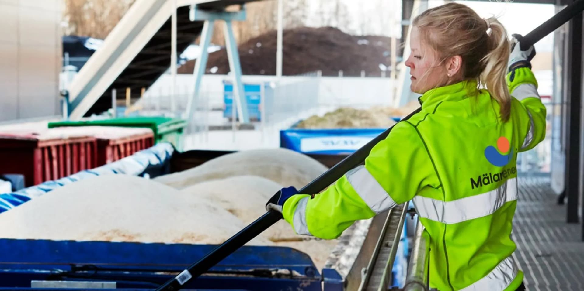 En kvinna i grön jacka som håller i en stor metallstång.