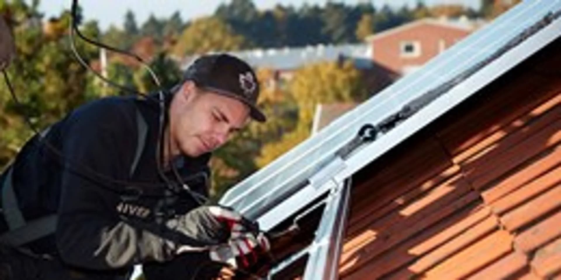 En man installerar solceller på taket till ett hus.