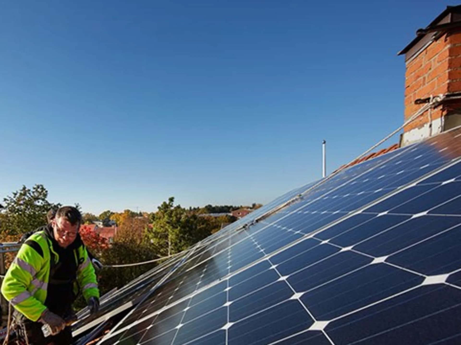 En man installerar solceller på taket till ett hus.
