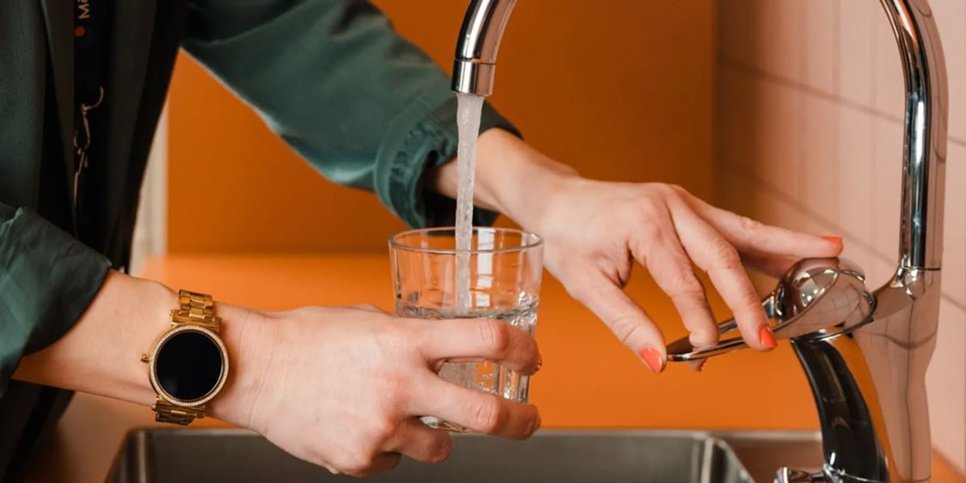 En kvinna fyller ett glas med vatten från en kran.