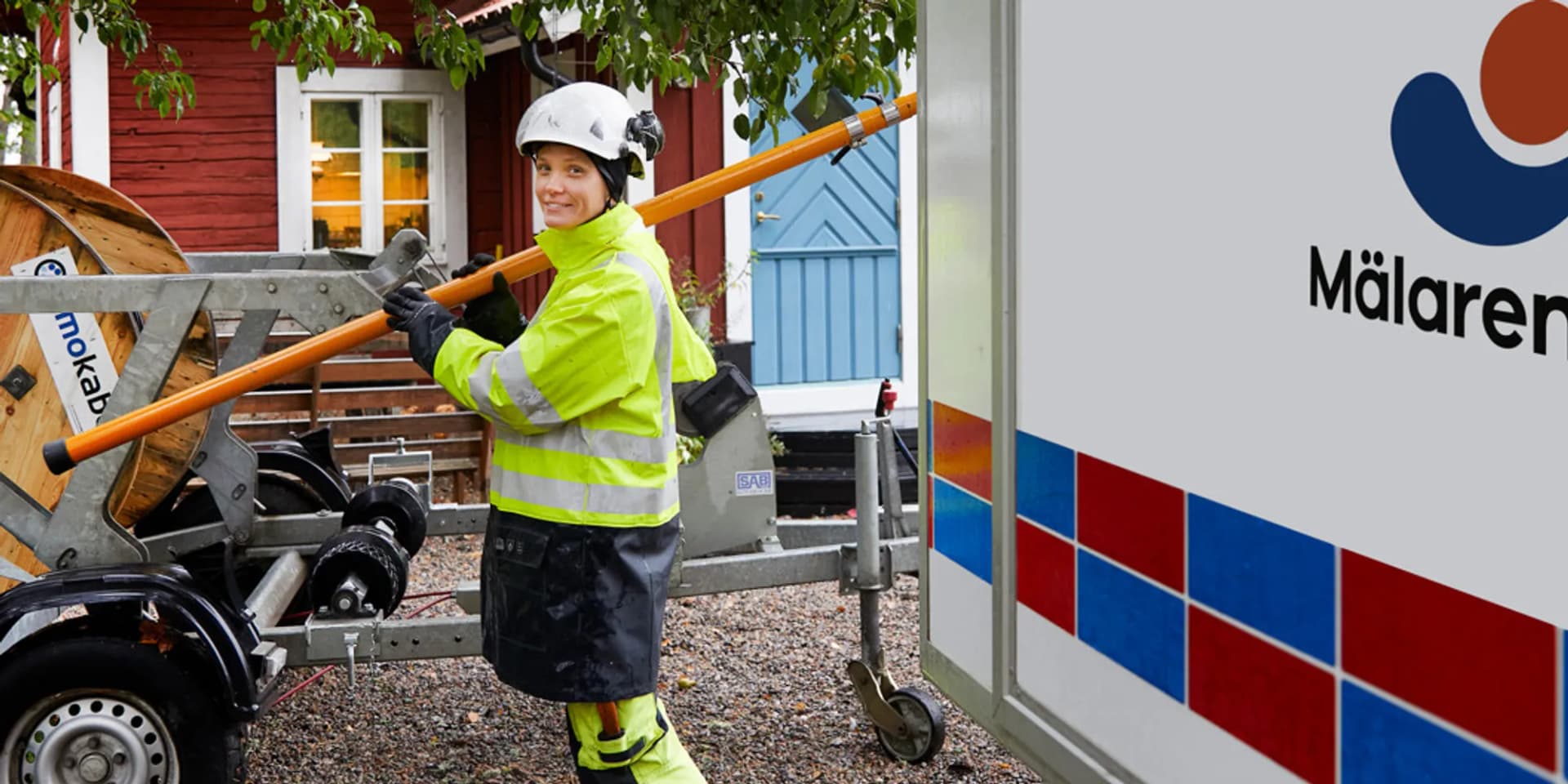 En kvinna i gul jacka håller i ett stort träföremål.