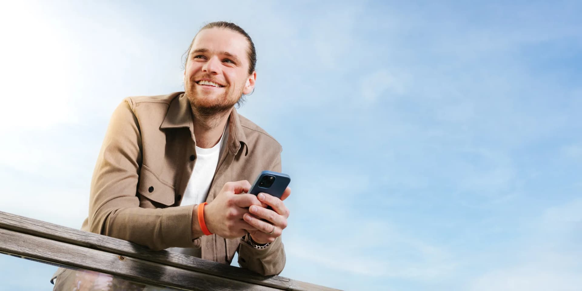 En man lutar sig mot ett räcke och håller i en mobiltelefon.