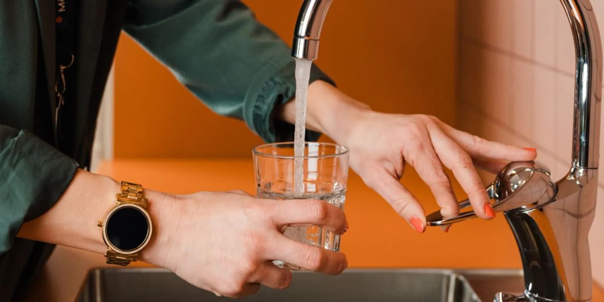 En kvinna fyller ett glas med vatten från en kran.