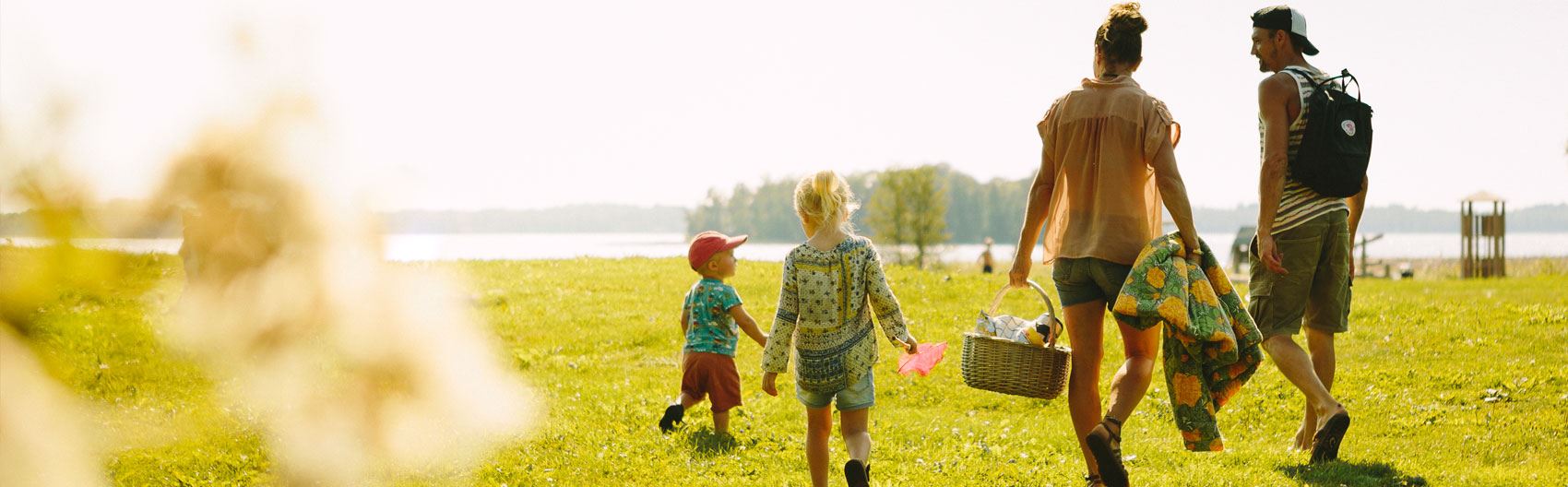 hallbarhetsredovisning_tema2 En familj med två vuxan och två barn som går över gräset ned mot vattnet.