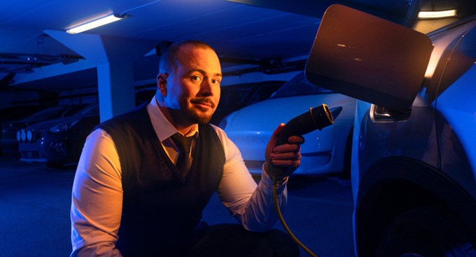 Person håller en laddkabel och kopplar in den i en elbil i ett parkeringsgarage med flera bilar runtomkring.