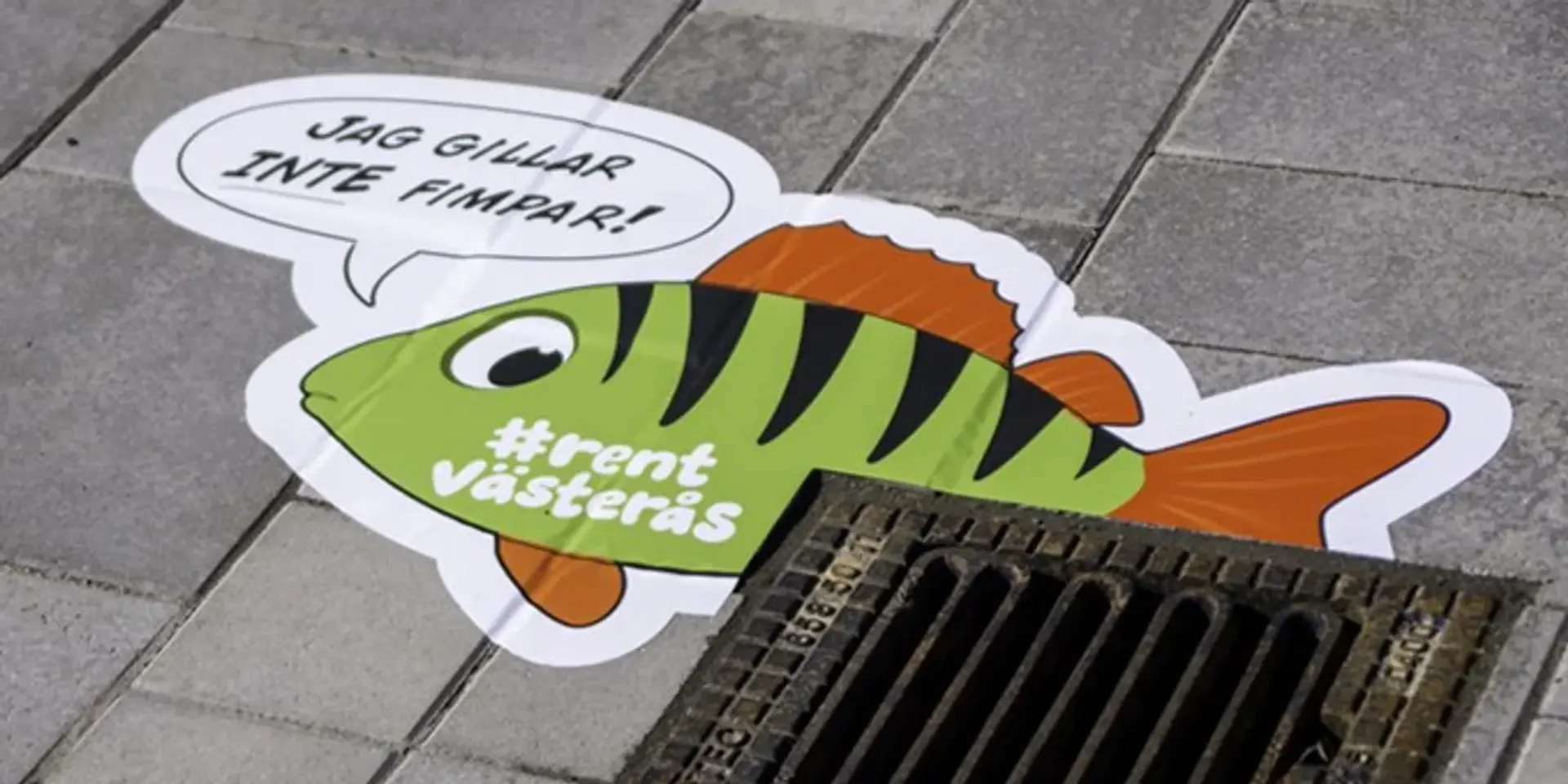 Ett klistermärke av en fisk på marken bredvid ett avlopp.