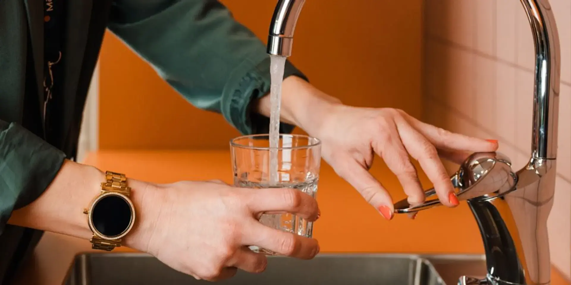 En kvinna fyller ett glas med vatten från en kran.