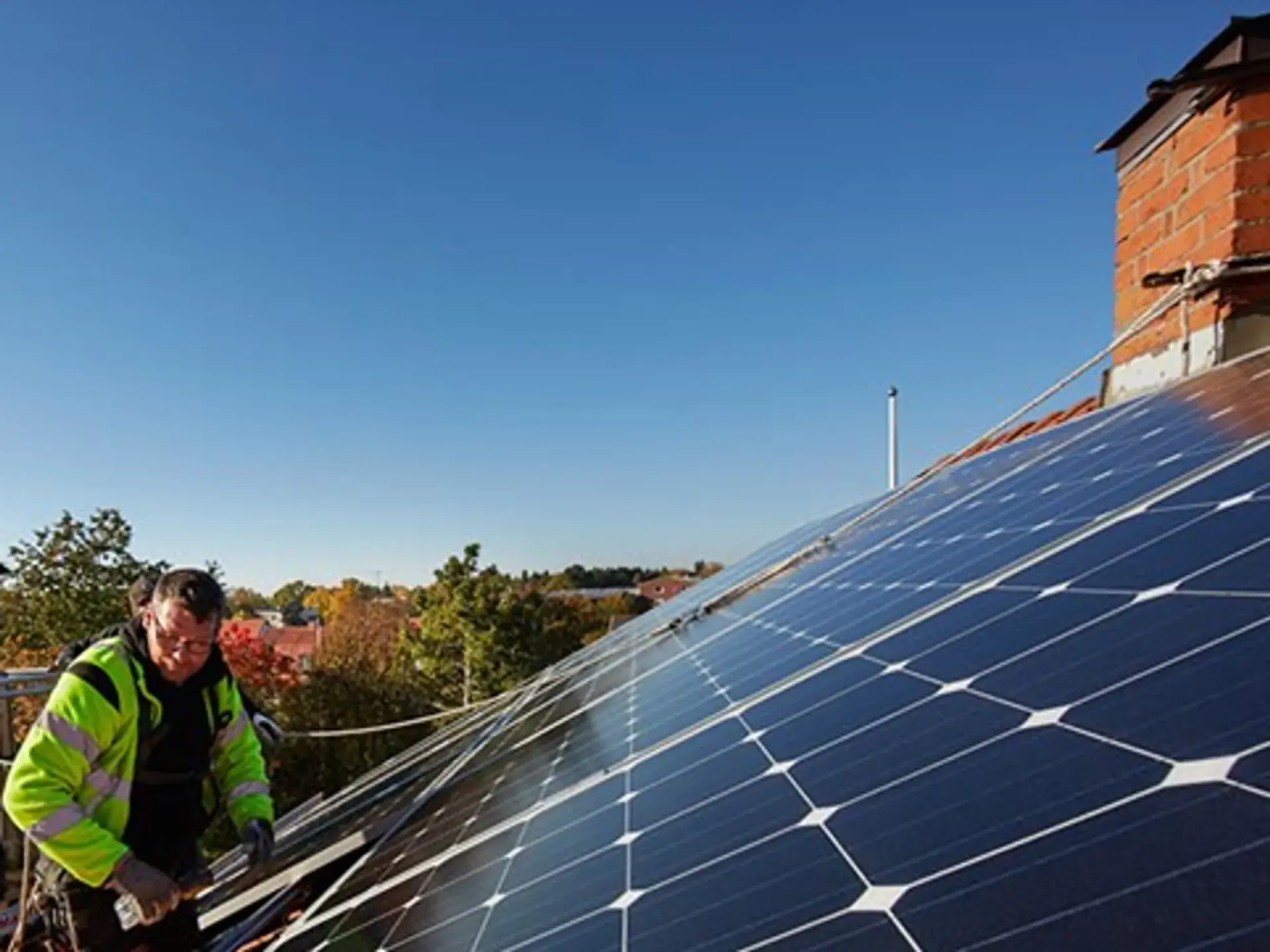 En man installerar solceller på taket till ett hus.